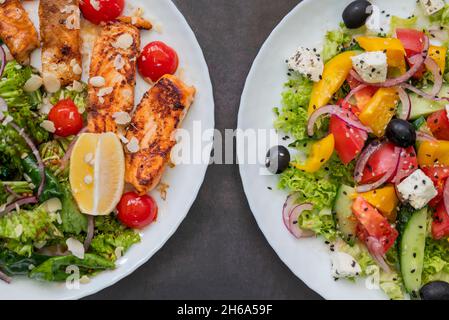 Blick von oben auf zwei griechische Salate mit Oliven und Feta-Käse und gebratenem Lachs Stockfoto