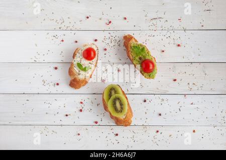 Drei hausgemachte helle Mini-Sandwiches mit Frischkäse und Gemüse, auf weißem Holzhintergrund, Draufsicht Stockfoto