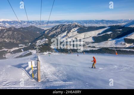 Slowakei. Winter Skigebiet Jasna. Sonniges Wetter und blauer Himmel über der Skipiste. Snowboarder im Schneetreiben und Panorama der Berggipfel auf dem hori Stockfoto