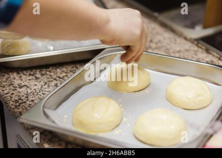 Vorbereiten von Burger-Buns, Herstellen von Burgern. Die Hände eines Küchenchefs, der Sesam auf Burger-Brötchen streut. Herstellung von Bastelbrötchen für Burger. Stockfoto