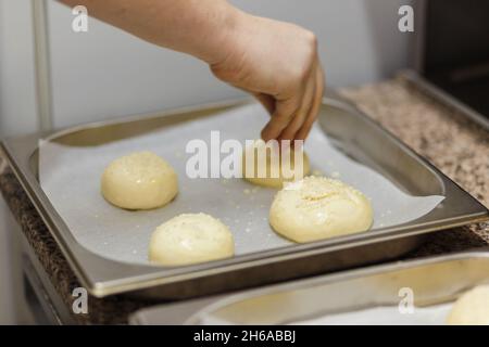 Vorbereiten von Burger-Buns, Herstellen von Burgern. Die Hände eines Küchenchefs, der Sesam auf Burger-Brötchen streut. Herstellung von Bastelbrötchen für Burger. Stockfoto