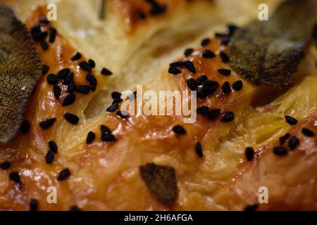 Nahaufnahme einer gebackenen Wurstrolle mit schwarzen Sesamsamen und Salbei Stockfoto