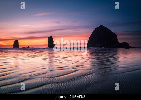 Wellen und Sonnenuntergänge vor dem Heuhaufen am Strand von Cannon Stockfoto