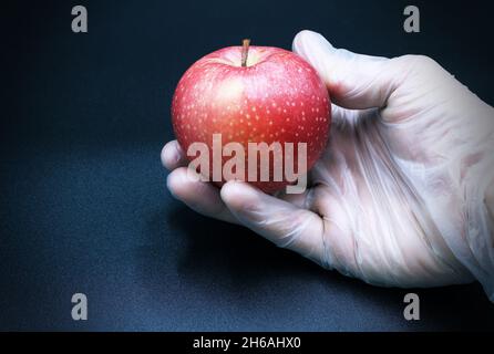 Hand trägt Latex mit einem roten Apfel auf schwarzem Hintergrund. Studioaufnahme. Stockfoto