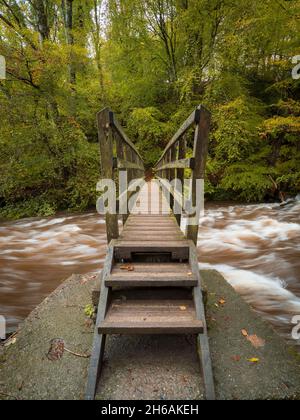 Eine alte Holzbrücke über einen rauschenden Fluss in Nordwales im Herbst Stockfoto