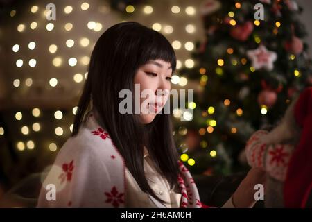 Eine junge, schöne koreanisch-asiatische Frau kleidet sich einen Weihnachtsbaum mit Spielzeug aus natürlichen Materialien im Stil von Zero Waste zu Hause mit positivem Stockfoto