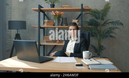 Der junge, attraktive Geschäftsmann ruht sich mit den Beinen auf dem Tisch von der Arbeit aus. Ein junger, vielversprechender Geschäftsmann trinkt mit angespreizten Beinen sorglos Kaffee Stockfoto