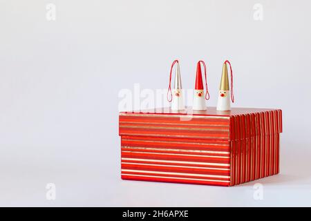 Drei Weihnachtsmänner-Figuren auf einer rot gestreiften Geschenkbox, weißer Hintergrund, Seitenansicht, Kopierbereich Stockfoto