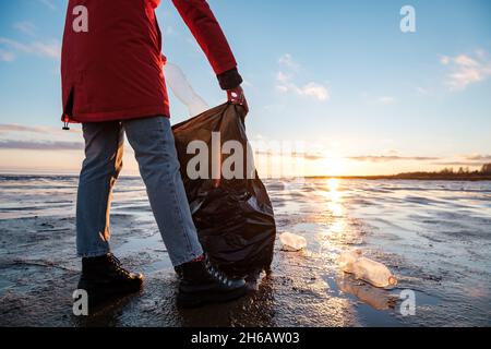 Eine Frau reinigt die Bank von Plastikflaschen und legt den Müll in einen Müllbeutel. Umweltverschmutzung durch Kunststoff. Wiederverwertbare Verpackung. Stockfoto