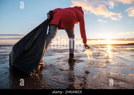 Eine Frau reinigt die Bank von Plastikflaschen und legt den Müll in einen Müllbeutel. Umweltverschmutzung durch Kunststoff. Wiederverwertbare Verpackung. Stockfoto