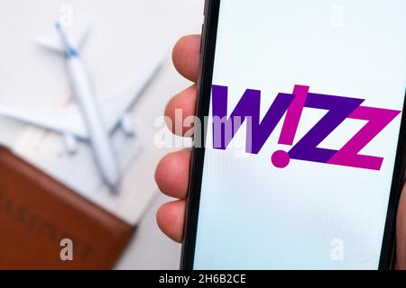 Wizz Airline Anwendung auf dem Smartphone-Bildschirm mans Hand. Ein weißes Spielzeugflugzeug und ein Reisepass liegen auf einem Tisch mit heller Oberfläche.November 2021, San Francisco, USA Stockfoto