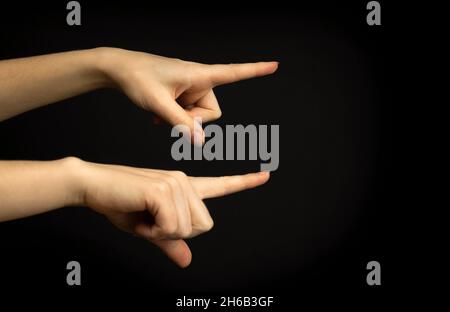 Hände zeigen auf etwas. Frau Handbewegung, zeigendes Zeichen, Geste Schauen Sie sich das an, Pass auf. Schwarzer Hintergrund Stockfoto