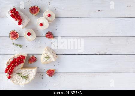 camembert und Ziegenkäse verziert mit Scheiben von Figuenfrüchten, roten Johannisbeeren und Rosmarin, auf weißem Holzhintergrund, Draufsicht, Kopierraum Stockfoto