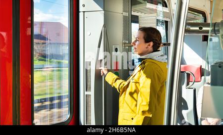 Eine Frau fährt mit einem Elektrozug, der sich am Handlauf hält. Das Mädchen steht in der Nähe der Ausgangstür des U-Bahn-Wagens. Vorteile der Fahrt mit der öffentlichen straßenbahn Stockfoto