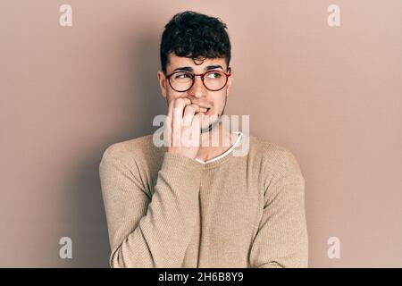 Junge hispanische Mann trägt Freizeitkleidung und Brille gestresst und nervös mit Händen auf Mund beißen Nägel. Angst Problem. Stockfoto