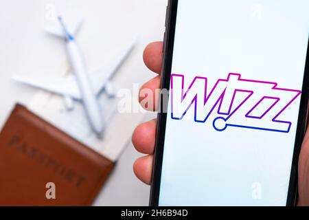 Wizz Airline Anwendung auf dem Smartphone-Bildschirm mans Hand. Ein weißes Spielzeugflugzeug und ein Reisepass liegen auf einem Tisch mit heller Oberfläche.November 2021, San Francisco, USA Stockfoto