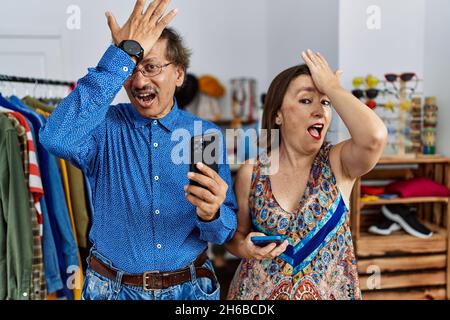 Interracial Paar im mittleren Alter im Einzelhandel mit Smartphone überrascht mit Hand auf Kopf für Fehler, erinnern Fehler. vergessen, schlechtes Gedächtnis-Konzept. Stockfoto