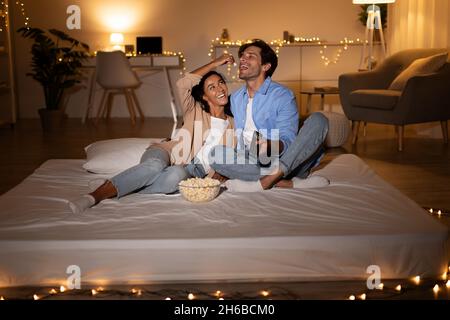 Paar Spaß beim Fernsehen Popcorn essen und sich gegenseitig füttern sitzen auf Matratze entspannen zu Hause am Abend. Ehepartner Verbringen Wochenende Toge Stockfoto