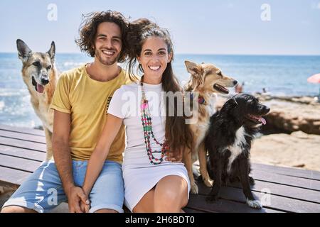 Mann und Frau Paar lächeln selbstbewusst und umarmen sich am Meer mit Hunden Stockfoto