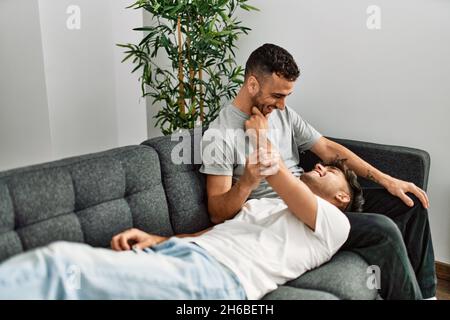 Zwei hispanische Männer, die zu Hause lächeln und selbstbewusst auf dem Sofa sitzen Stockfoto