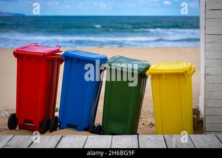 Bunte Mülltonnen am Sonnenstrand mit dem Meer im Hintergrund Stockfoto