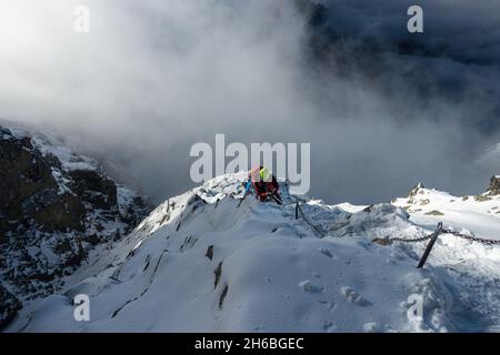 Kletterer, der auf eisigen Felsen hochklettert, während er Kette hält, über den Klettersteig in der Hohen Tatra auf dem Weg zum Rysy-Gipfel. Stockfoto