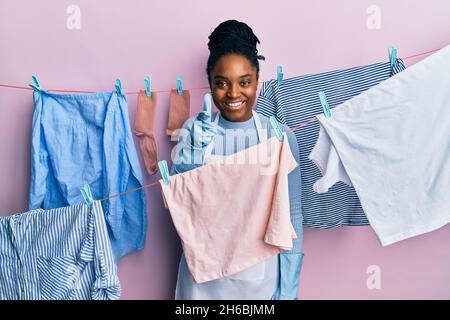 afroamerikanische Frau mit geflochtenen Haaren waschen Kleidung an Wäscheleine zeigt Finger zur Kamera mit glücklichen und lustigen Gesicht. Gute Energie und Vibes. Stockfoto