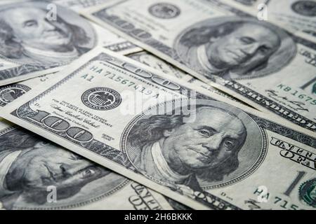 Ein Teil der US-Dollar-Rechnung in Höhe von 100 US-Dollar mit einem dramatischen Schatten, der über dem Haufen anderer Barmittel zu sehen ist. Selektiver Fokus. Konzept für Finanzen und Investitionen Stockfoto