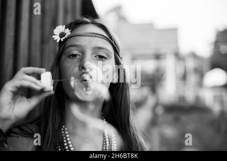 Ein Mädchen in Hippie-Kleidung im Dorf bläst Seifenblasen. Schwarzweiß-Foto. Stockfoto