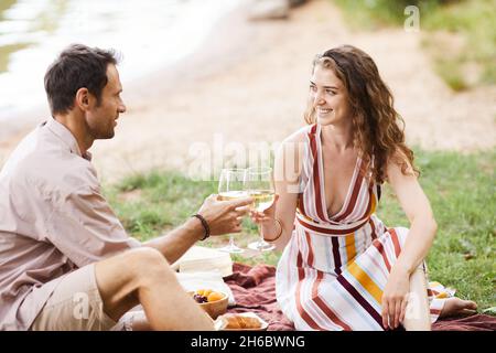 Porträt eines glücklichen jungen Paares, das Weingläser hält, während es ein romantisches Picknick im Freien genießt, Platz zum Kopieren Stockfoto