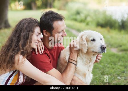 Seitenansicht Porträt eines glücklichen jungen Paares mit Hund auf grünem Gras im Freien sitzen Stockfoto