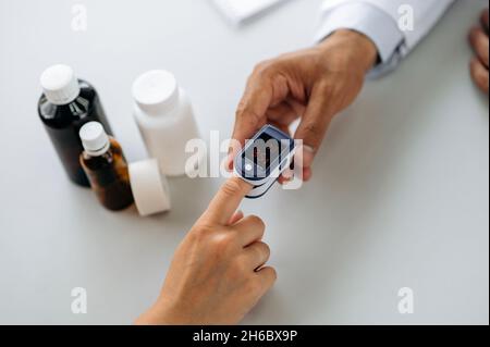 Apparate zur Messung der Sauerstoffsättigung und des Pulses. Der Arzt misst die Sauerstoffsättigung und den Puls des Patienten während einer Erkrankung, indem er ein Pulsoximeter auf seinen Finger legt. Draufsicht Stockfoto