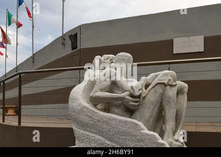 Eine Marmorstatue im Hafen von Porto Luca Ferrari von Alassio mit EU-Flaggen im Hintergrund, Alassio, Savona, Ligurien, Italien Stockfoto