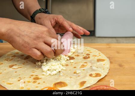Der Koch legte den gekochten Schinken mit den Händen über den gehackten frischen Käse in eine salzige Kreppe Stockfoto