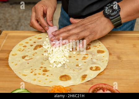 Hände eines männlichen Küchenchefs mit schwarzer Uhr, die ein salziges Crepe mit Käse und gekochtem Schinken zubereitet Stockfoto