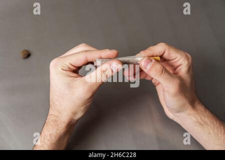 Erwachsener Mann rollt gemischten Tabak mit Filter auf dem grauen Tisch Stockfoto