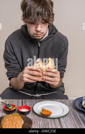 Männlicher Teenager, der einen Rinderburger mit Käse auf einem Holztisch isst Stockfoto