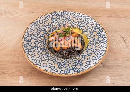 Tintenfisch-Risotto nero, geschmort mit roten Zwiebeln und zerschlackten Tintenfischringen auf einem in Blau und Weiß verzierten Porzellanteller Stockfoto