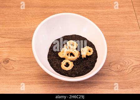 Köstliches italienisches Rezept für Risotto nero mit Tintenfischringen, gekrönt mit Mehl und Ei auf einer weißen Schüssel Stockfoto