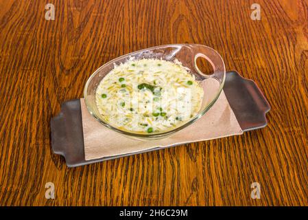 Italienisches Risotto-Rezept mit Erbsen und frischem Käse auf einer transparenten Glasschüssel Stockfoto