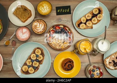 Bild von oben mit gesunden Gerichten zum Frühstück und Desserts. Acai mit roten Früchten, Toast mit Bananen und roten Früchten, Biskuit, Joghurt Stockfoto