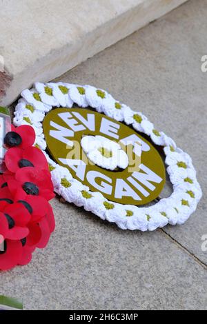 London, Großbritannien. Ein weißer Mohn-Kranz mit den Worten: 'Nieh wieder', neben einem traditionellen Kranz, der am Gedenktag im Cenotaph platziert wurde. Stockfoto