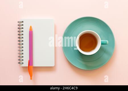 Leerer Notizblock und Tasse Tee auf rosa Hintergrund. Arbeitsbereich. Draufsicht Stockfoto