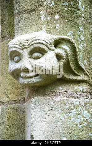 An einer Steinsäule an der Außenseite der Ruinen des Teils der Kirche Saint Saveur in Locmine, Bretagne, ist ein heiteres, geschnitztes Gesicht zu sehen. Stockfoto