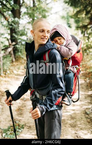 Mann Reisende mit müdem Kind im Rucksack Vater trägt seine Tochter in einem Rucksack Männlich nahm rutschenden Kind in die Berge. Reisen mit Kindern Stockfoto