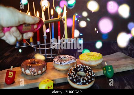 Happy Hanukkah und Hanukkah Sameach - traditioneller jüdischer Kerzenständer mit Kerzen, Donuts und Spinning Tops auf braunem Holzhintergrund. Stockfoto