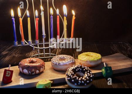 Happy Hanukkah und Hanukkah Sameach - traditioneller jüdischer Kerzenständer mit Kerzen, Donuts und Spinning Tops auf braunem Holzhintergrund. Stockfoto