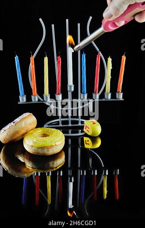 Happy Hanukkah und Hanukkah Sameach - traditioneller jüdischer Kerzenständer mit brennenden Kerzen und Donuts vor schwarzem Hintergrund mit Spiegelung. Stockfoto