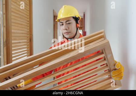 Serious Stirnrunzeln Baumeister trägt Holzgitter an der Wand im Haus zu installieren Stockfoto