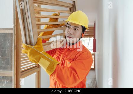 Porträt eines ernsthaften Bauarbeiters, der schwere Holzroste trägt, wenn er durch den Flur im Haus geht Stockfoto